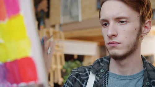 Close-up Portrait of Young Man Artist Painting Picture in Studio Looking at Canvas