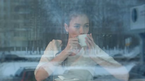 Dreamy Young Woman with a Cup of Tea at a Cafe Watching City Life