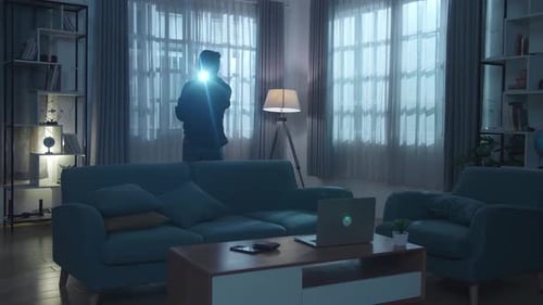 Burglar shines flashlight in dark house at night