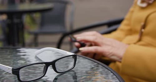 Close-up of Glasses Lying on the Table in the Background Female Hands Using Phone on Social Network