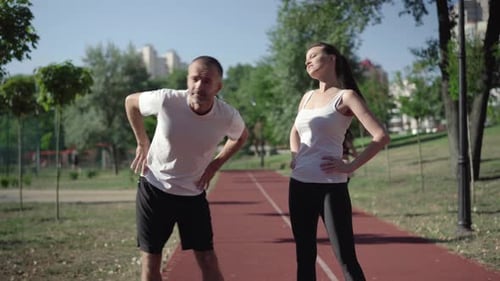 Retrato de una pareja adulta caucásica en forma que termina el ejercicio de calentamiento y huye en un campo deportivo