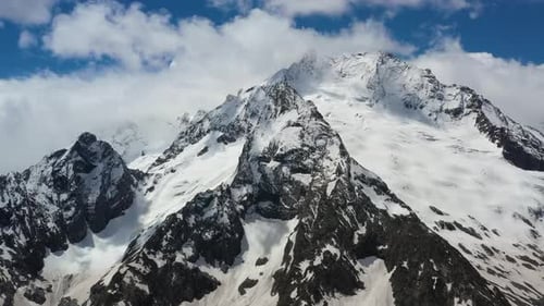 Air Flight Through Mountain Clouds Over Beautiful Snowcapped Peaks of Mountains and Glaciers