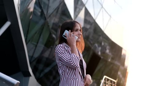 Beautiful Girl Talking on a Mobile Phone Outdoors Near a Modern Building