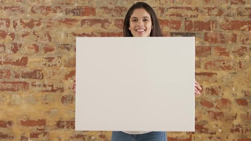 Mujer caucásica que sostiene un rectángulo blanco en una pared de ladrillos