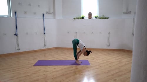 Flexible woman performing Standing Forward Bend pose on yoga mat