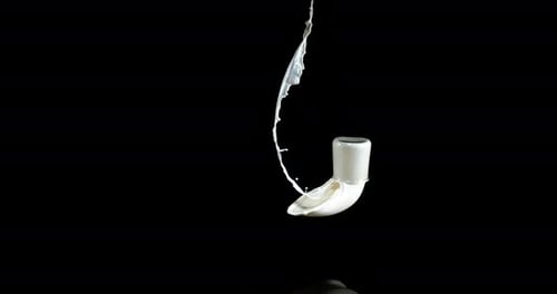 Vaso de leche rebotando y salpicando sobre fondo negro, cámara lenta 4K