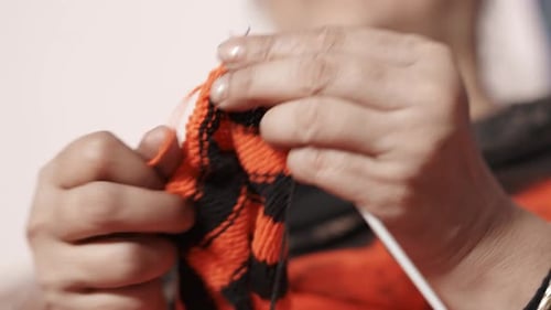 Indische Frau strickt einen Schal mit roter und schwarzer Wolle und zwei Nadeln. Nahaufnahme der Strickarbeit t