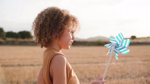 Close up shot of young boy with cool hairs spinning windmill standing in sunlight during sunset.