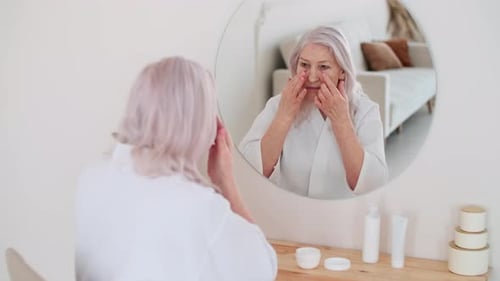 Senior Woman Applies Cream in Mirror