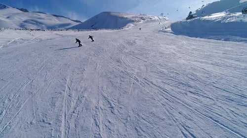 Snowboarders Carving Down Snowy Mountain Slope in Winter