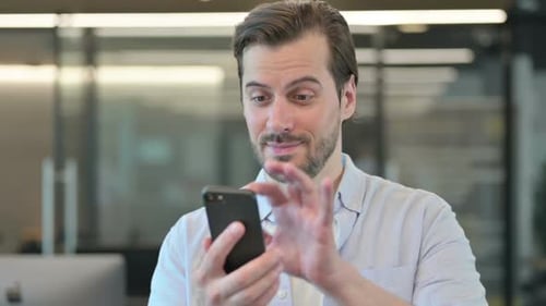 Man Celebrates Success on Smartphone in Office