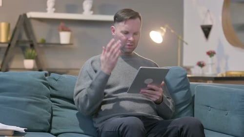 Man Using Tablet Sitting on Couch Indoors