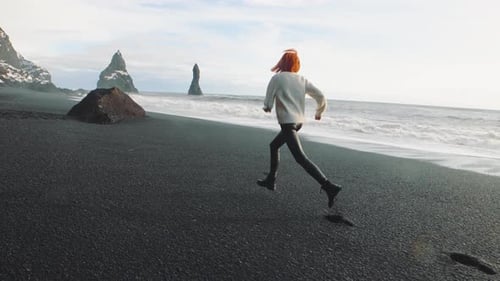 Yong Redhaired Woman Traveler Running on Volcanic Black Sand Beach in Iceland