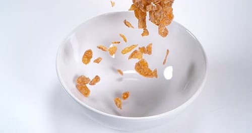 Crispy Corn Flakes Falling into a White Bowl