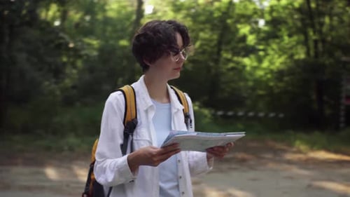 Tourist View Of The Road In The Forest, Travel Lifestyle. A Girl With A Backpack Holds A Map. Woman