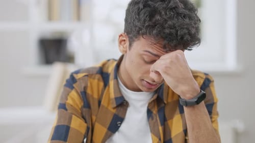 Exhausted Middle Eastern Teen Boy with Migraine Rubbing Eyes and Putting on Eyeglasses Sitting