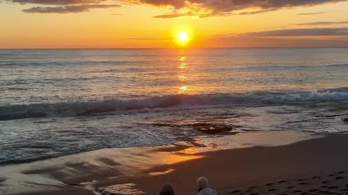 People sit on the beach and watch the sunset