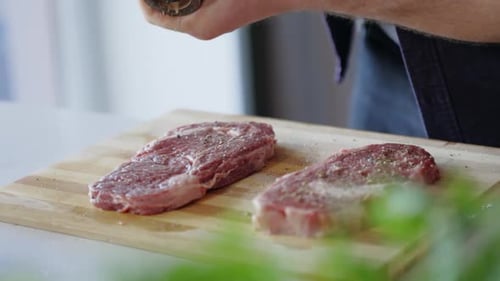 Man Seasoning Two Raw Steaks in Kitchen