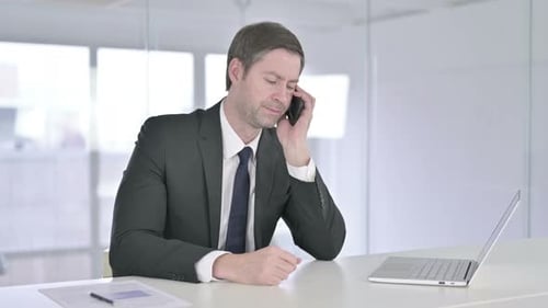 Serious Middle Aged Businessman Talking on Smartphone in Office