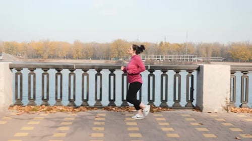 Woman Runs Along Paved Riverfront Path in Autumn