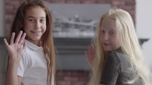 Two Smiling Girls Waving Indoors
