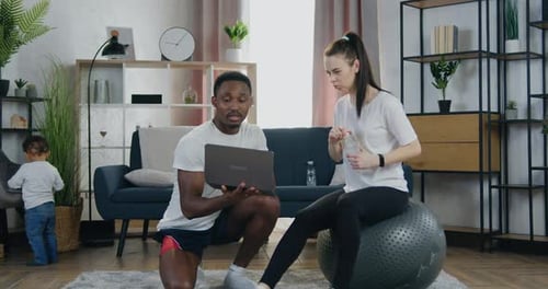 Pareja que hace una pausa en el entrenamiento conjunto, hombre busca entrenamiento en Vídeo en una computadora portátil mientras es mujer