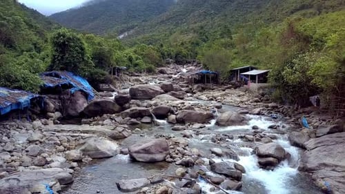 Drone Flies Close To Rocky River with Boulders and Poor Houses