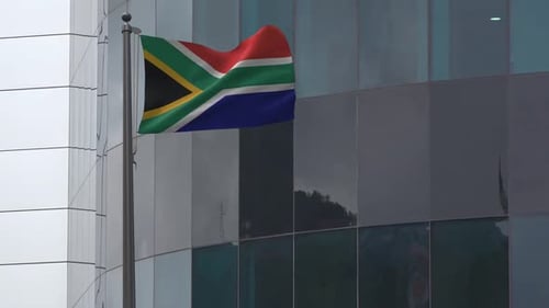 South African Flag Waving on Flagpole Against Modern Building