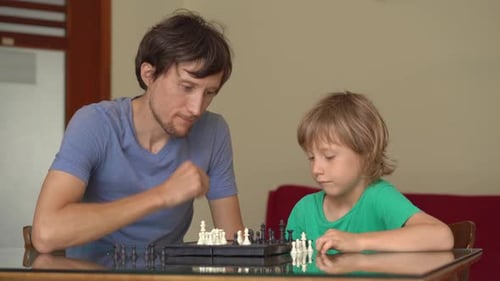 Young Man and His Son Play Chess at Home During the Quarantine. Self-isolation with Kids