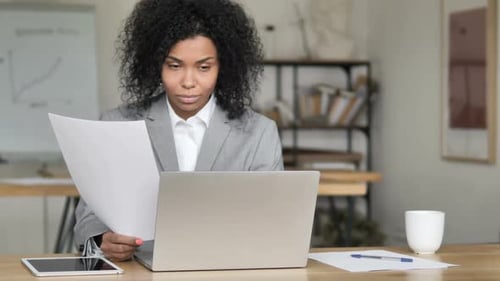 Woman in Office Reading Document at Computer