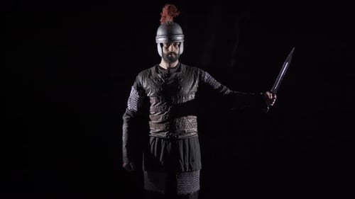 Man in Armour Holding Sword in Dark Setting