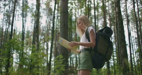 Young Caucasian Woman Looking for Direction on a Map While Hiking in the Forest. Happy Girl While