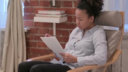 Woman Reviews Documents in Chair with Pen