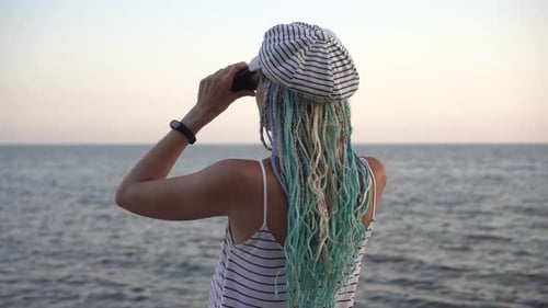Eine junge Frau schaut mit einem Fernglas auf das Meer