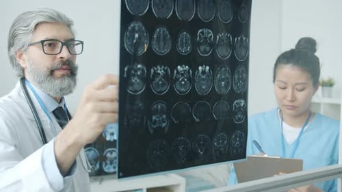 Doctor in White Coat Analyzing MRI Brain Images and Talking to Nurse in Scrubs Working in Clinic