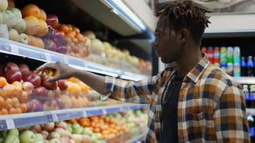 Handsome African American Man Standing in Supermarket and Choosing Apples