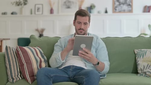 Man Relaxing on Sofa Using a Tablet