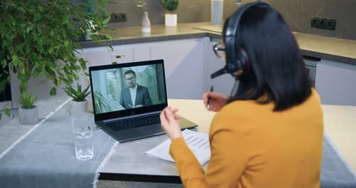 Mujer con auriculares realizando videoconferencia con un colega masculino