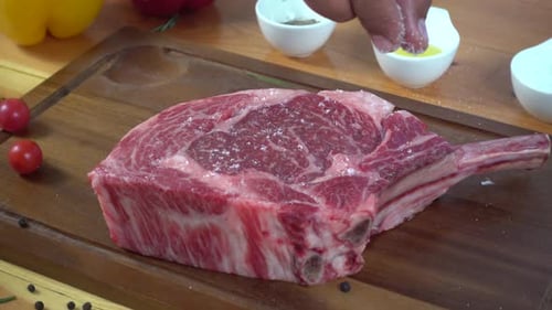 Chef cook season fresh chunk of deli piece of beef with sea salt and grounded spicy peppers.