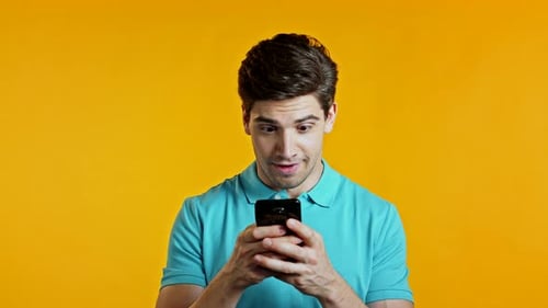 Handsome Man Receives Happy Notification on Mobile Phone. Guy Is Beside Himself with Surprise and
