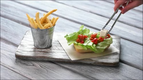 Hand with Tongs prepara la hamburguesa