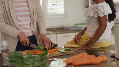 Woman Cutting Vegetables with Girl in Kitchen