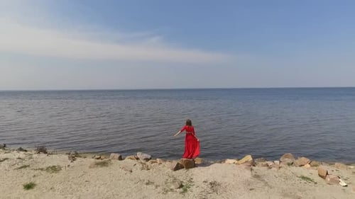 Woman in Red Dress Stands on Sandy Beach