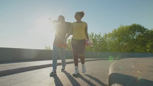 Two Young Women Walking with Skateboards on Path
