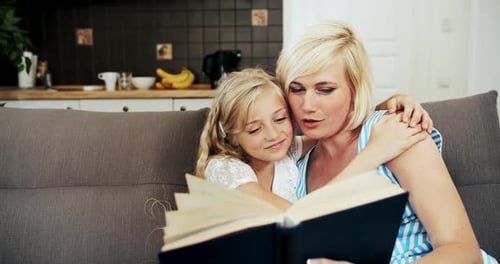 Happy Mother and Daughter Reading Book on Couch