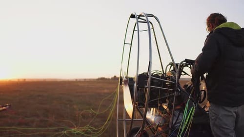 Man Pilot Motor Paraglider Fixes the Parachute To the Body of the Paraglider at Sunset in the Field