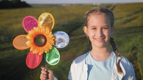 Happy Girl Holding Wind Toy in Green Field, Rejoicing Life. Cheerful Child in the Meadow with Wind