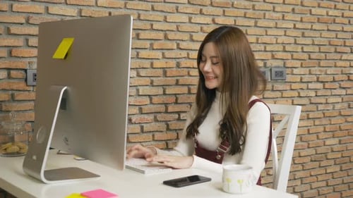 Smiling Asian business woman, young person working from home, typing on a keyboard