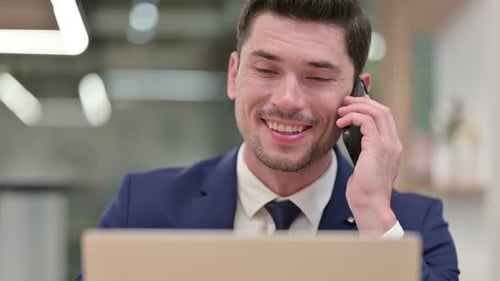 Close Up of Businessman Talking on Smartphone with Laptop