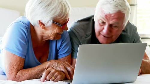 Elderly Couple Using Laptop Computer Together on Bed